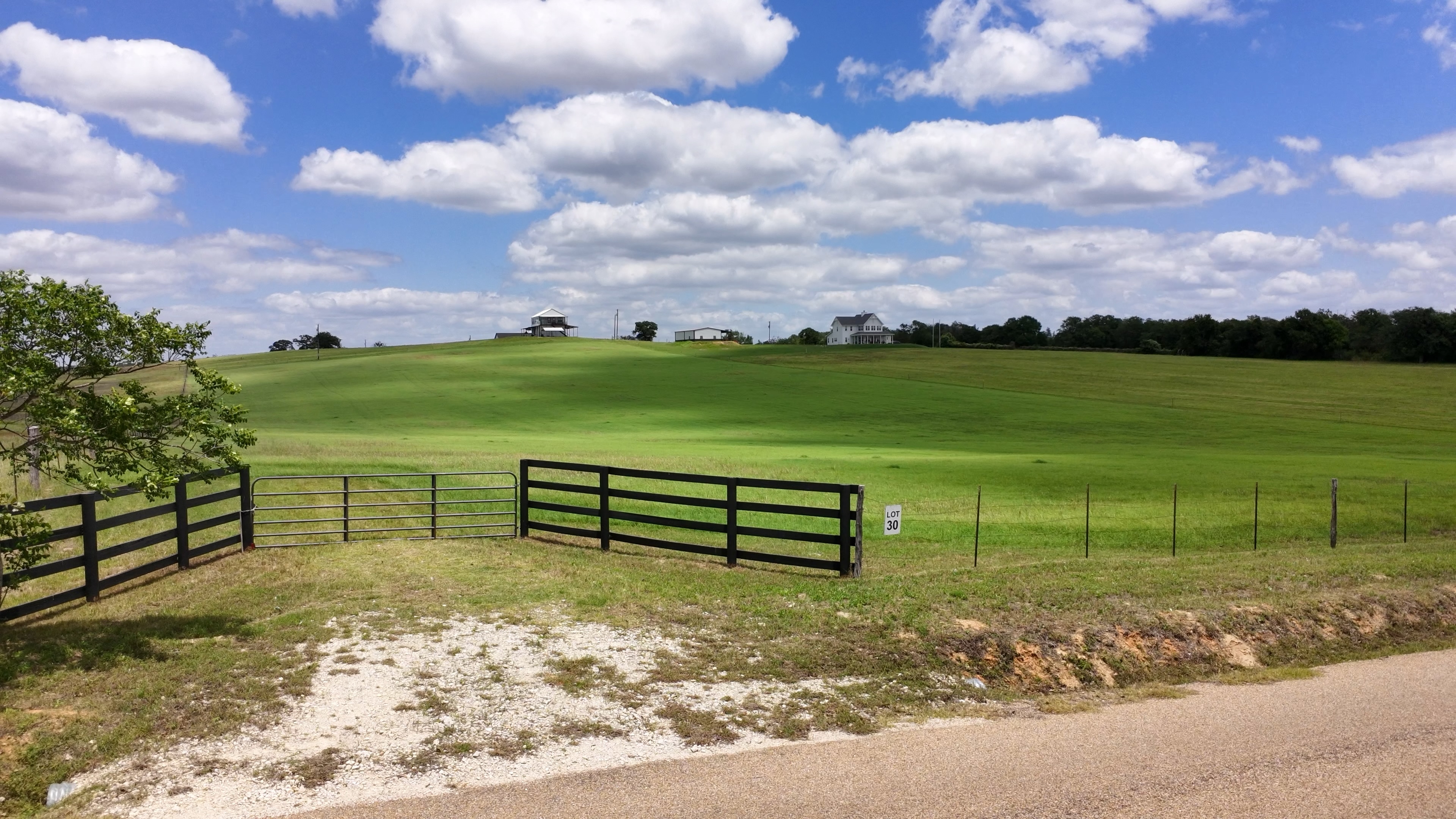 Property entrance gate with rolling green pasture and farmhouse on the hill
